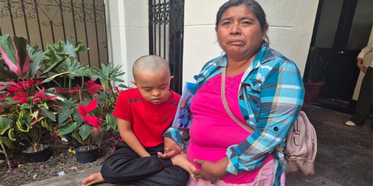 Madre con hijo en hospital infantil esperando apoyo para transporte